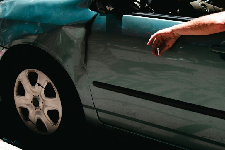 Close-up of a car door with visible damage and a hand resting on the edge.