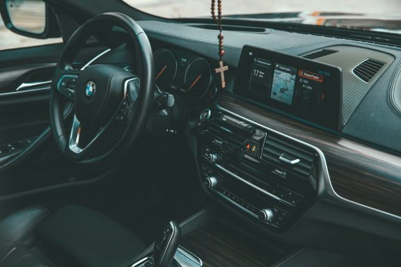 Interior of a BMW car featuring a steering wheel, dashboard, and a crucifix.
